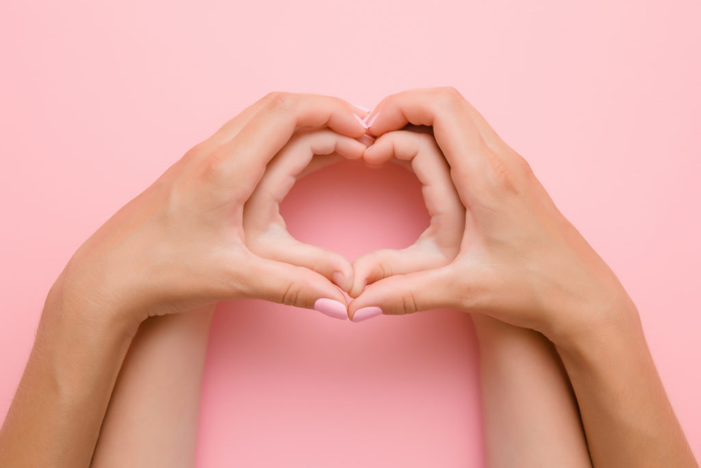 Heart shape created from little girl's hands and her mother's hands on the pink background